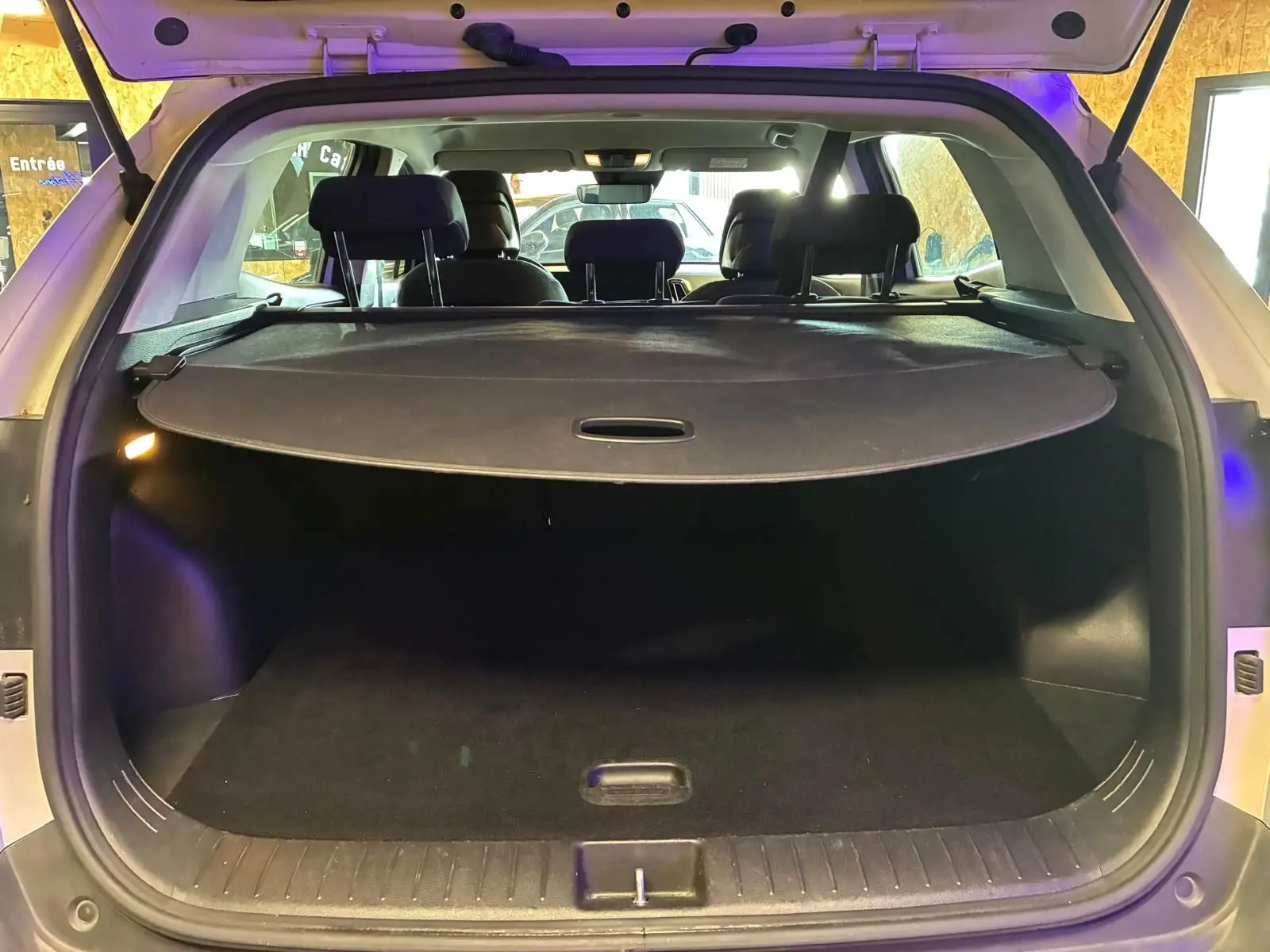 Vue arrière du coffre ouvert du KIA Sportage gris 2024, montrant l'espace de chargement avec cache-bagages déployé.