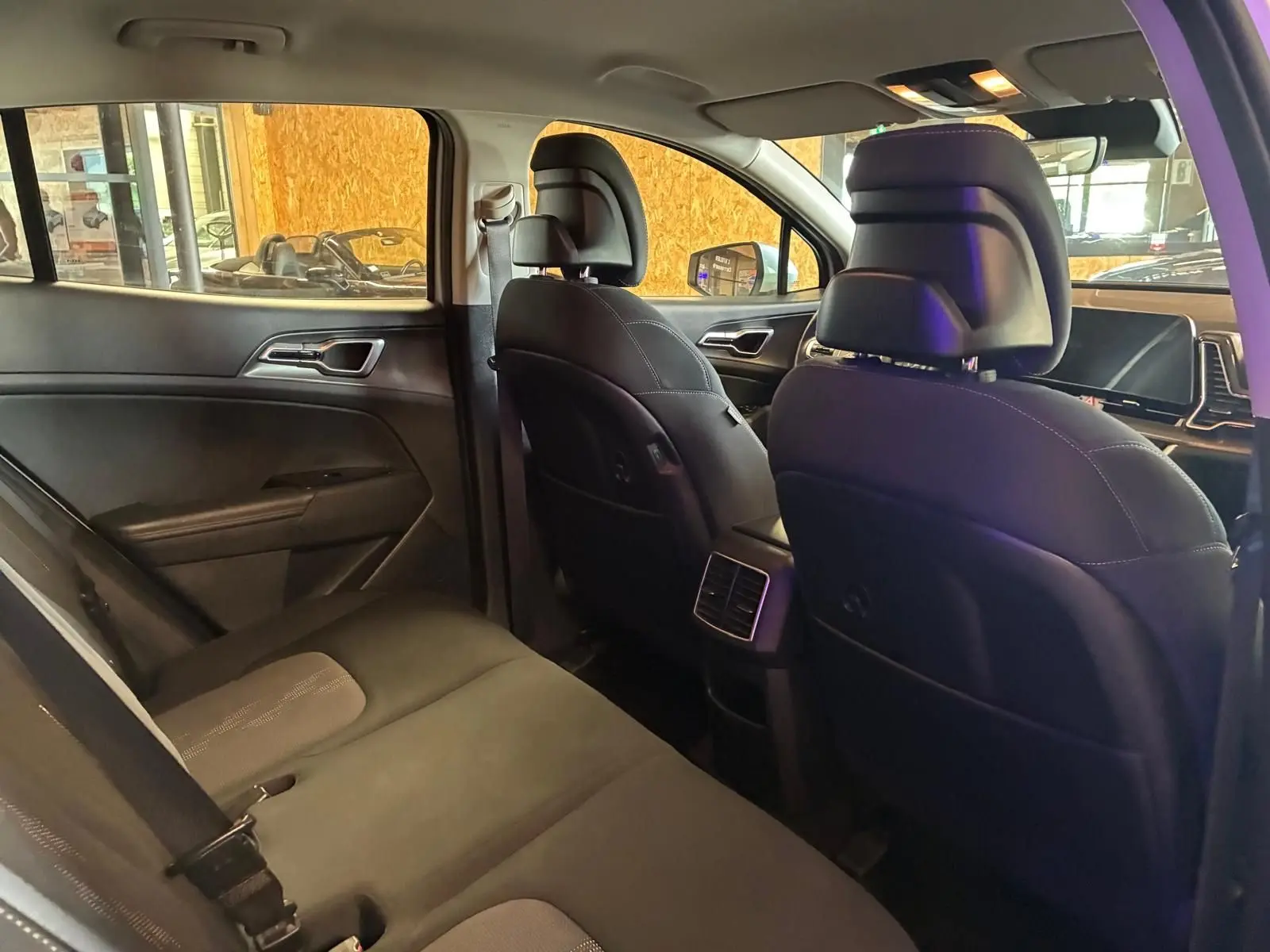 Vue intérieure arrière du Kia Sportage 2024 hybride, sièges noirs avec surpiqûres et aérateurs centraux visibles.