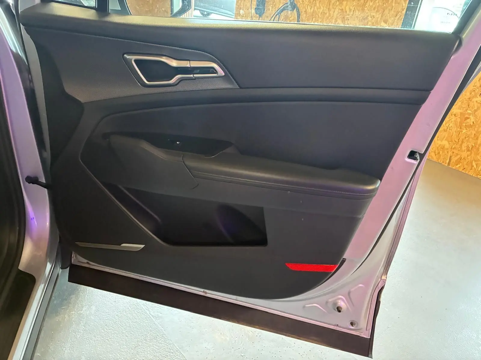 Vue intérieure de la porte avant gauche d’un KIA Sportage gris 2024, avec garniture noire et poignée argentée.