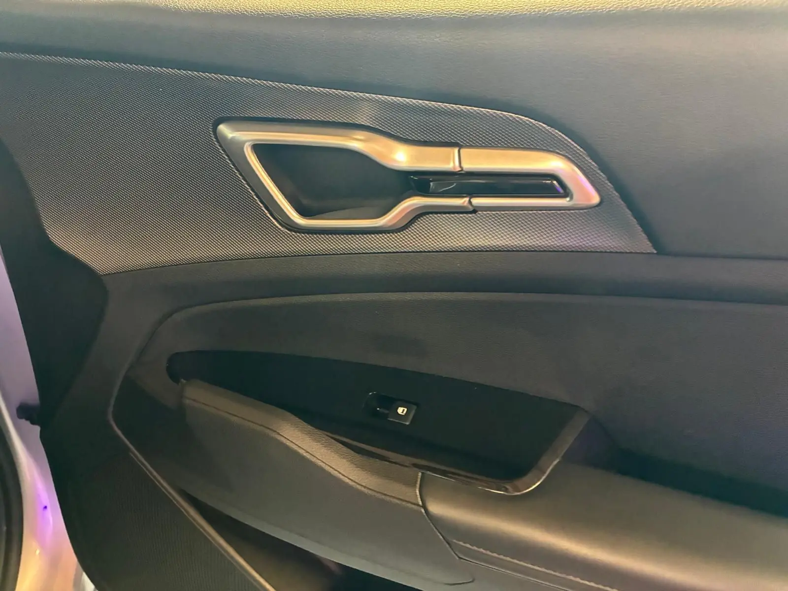 Détail de la poignée intérieure et commande de fenêtre côté gauche du KIA Sportage hybride gris 2024.