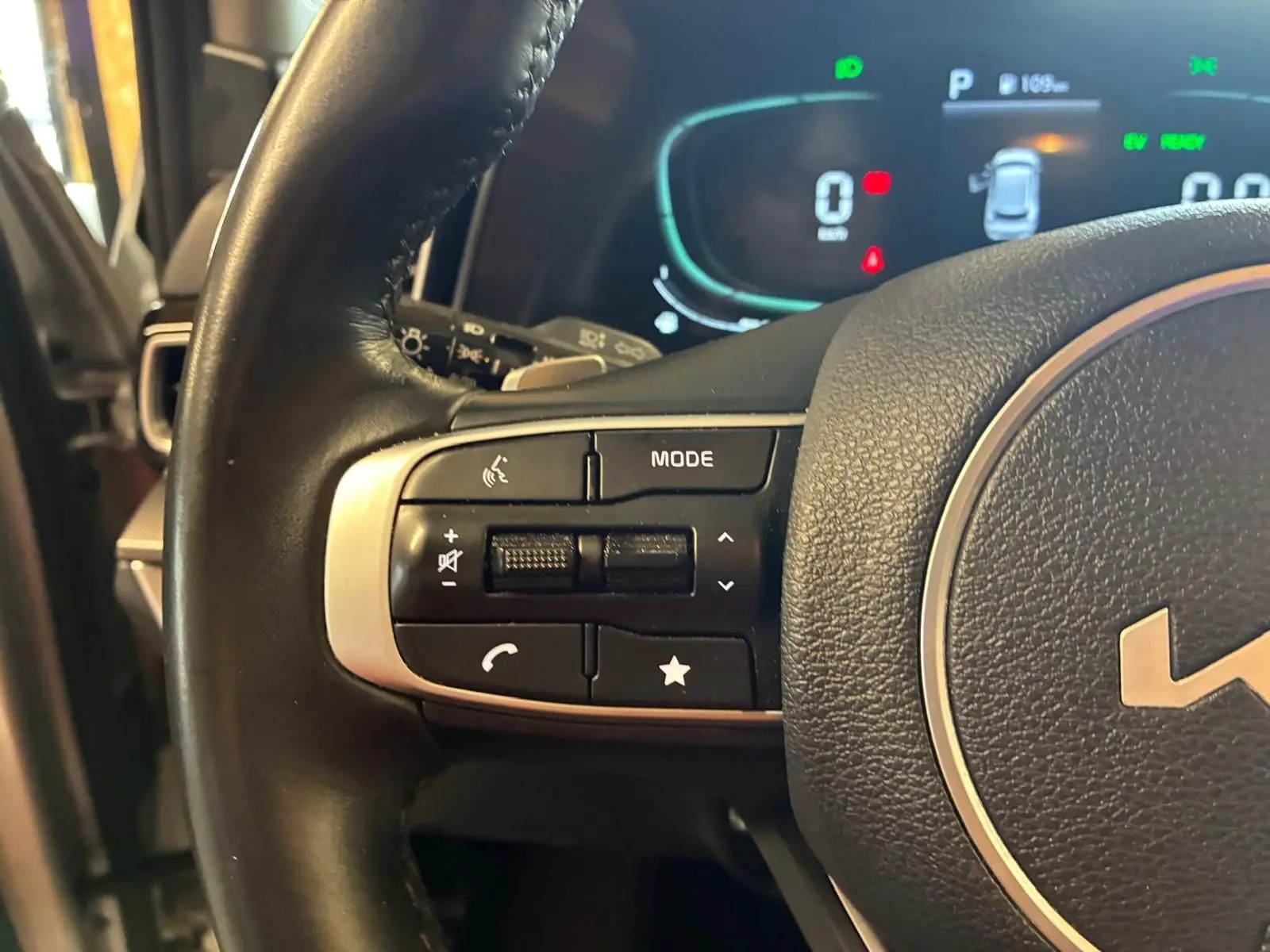 Gros plan sur les commandes gauche du volant du Kia Sportage hybride gris 2024 avec tableau de bord numérique en arrière-plan.