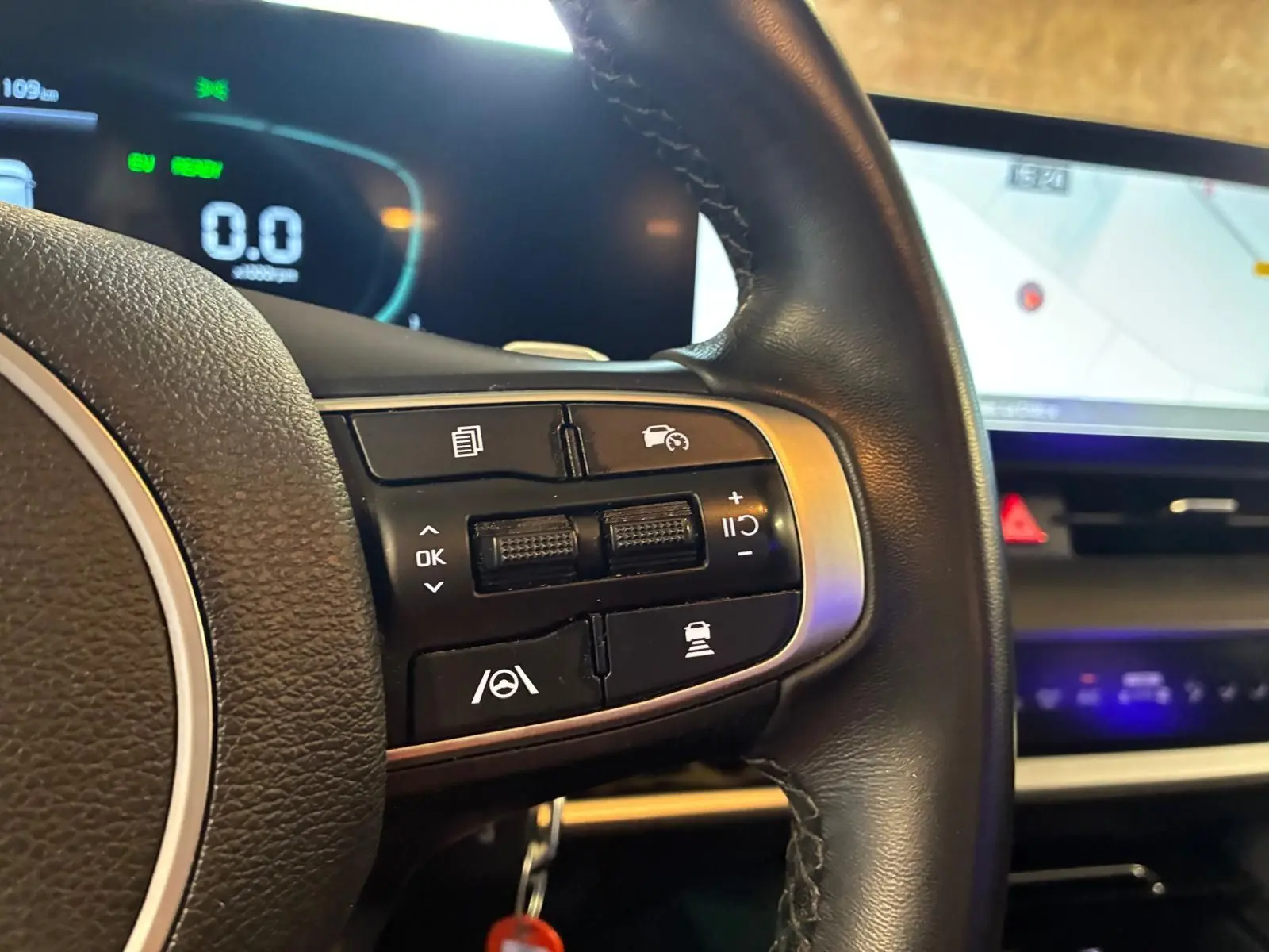 Gros plan sur le volant noir du Kia Sportage hybride 2024, avec commandes de régulateur et affichage numérique en arrière-plan.