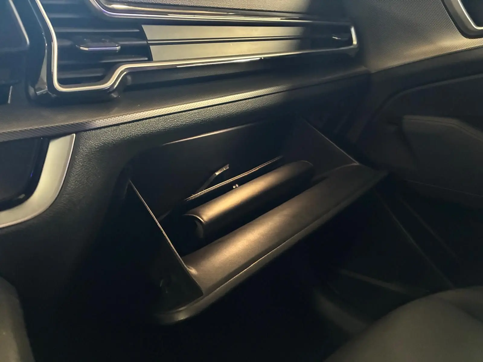 Gros plan sur la boîte à gants ouverte du Kia Sportage hybride gris 2024, côté passager avec tableau de bord noir.
