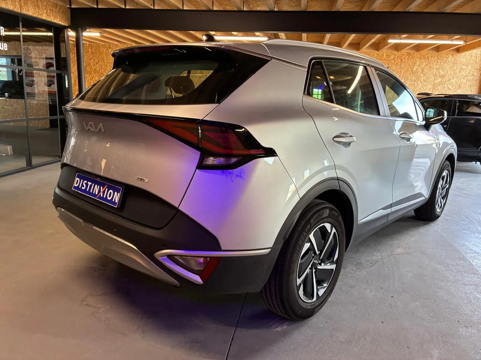 Vue 3/4 arrière droite d'un Kia Sportage gris hybride 2024 avec feux arrière distinctifs et jantes modernes.
