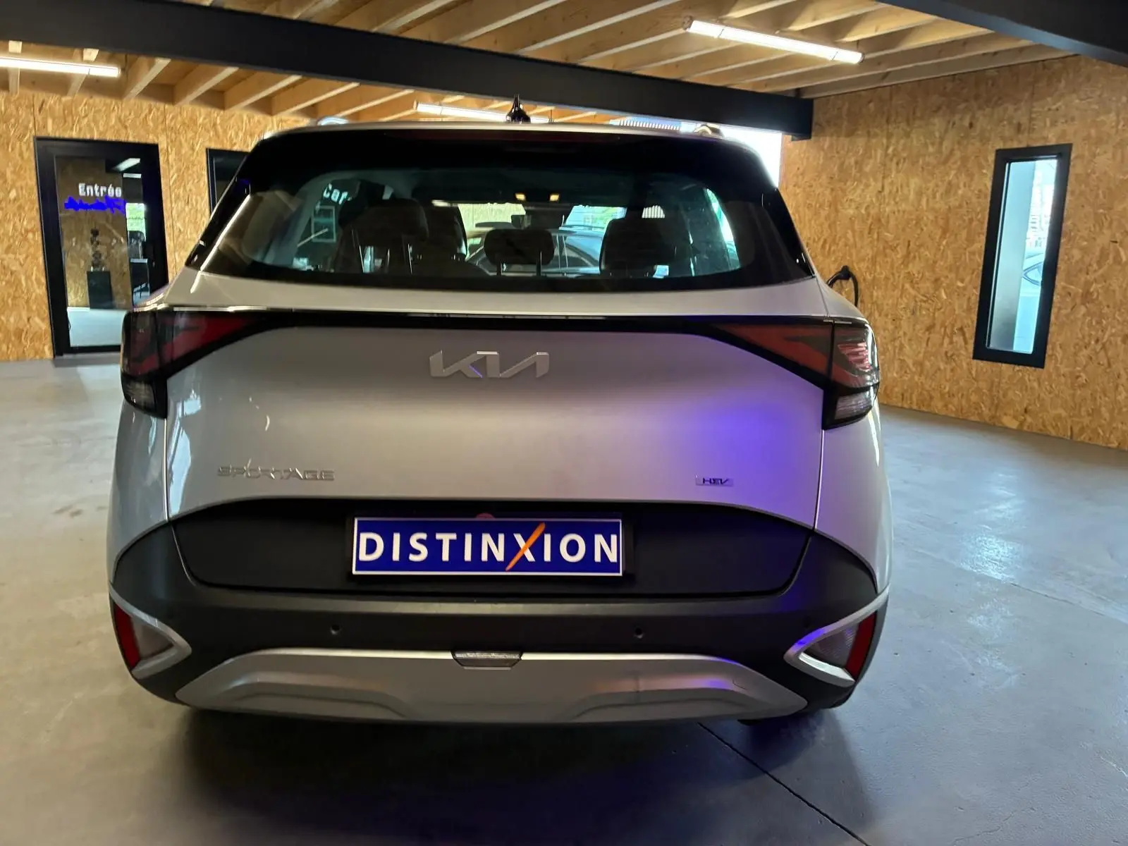 Vue arrière d’un KIA Sportage gris 2024 hybride, avec feux arrière reliés par une bande noire distinctive.