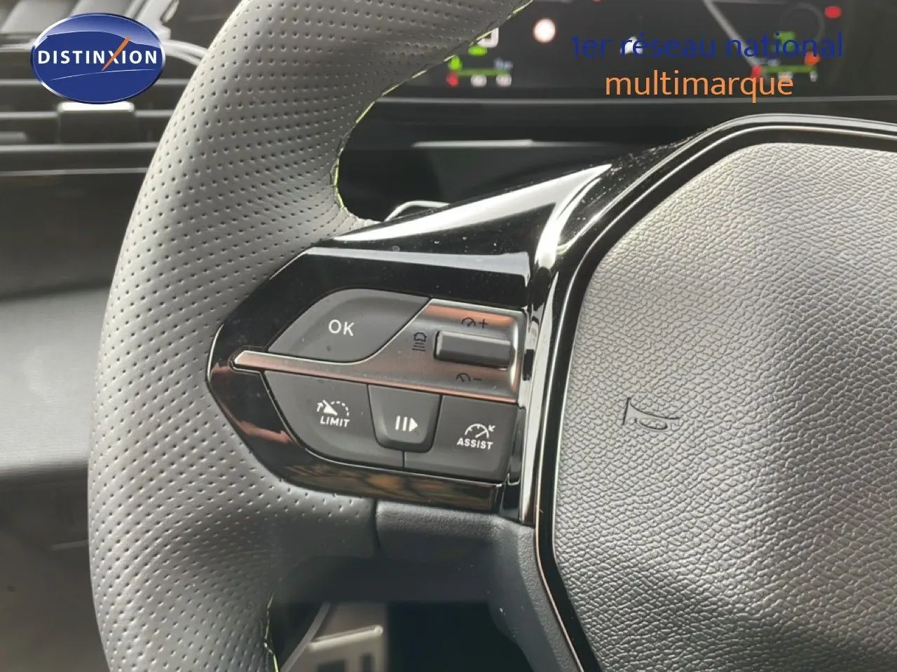 Gros plan sur le volant perforé de la Peugeot 308 gris selenium, avec commandes intégrées et tableau de bord en arrière-plan.