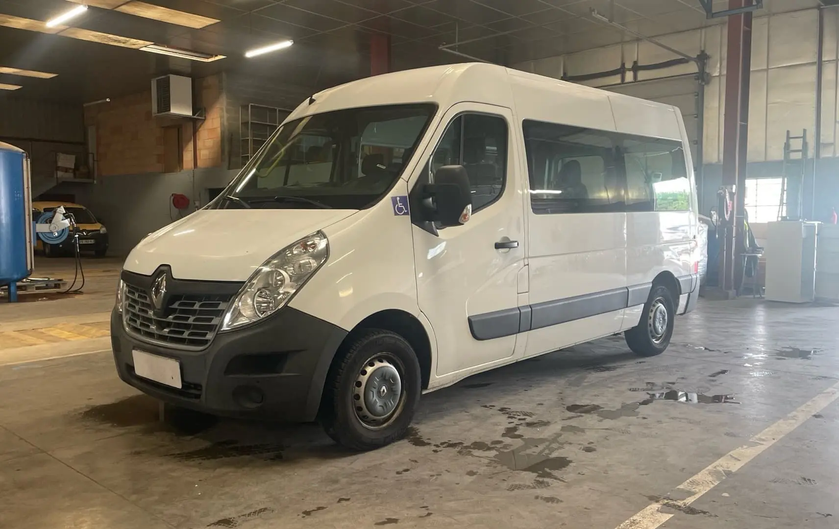 Renault Master blanc vu en 3/4 avant droit dans un garage, avec logo handicap sur la porte côté conducteur.