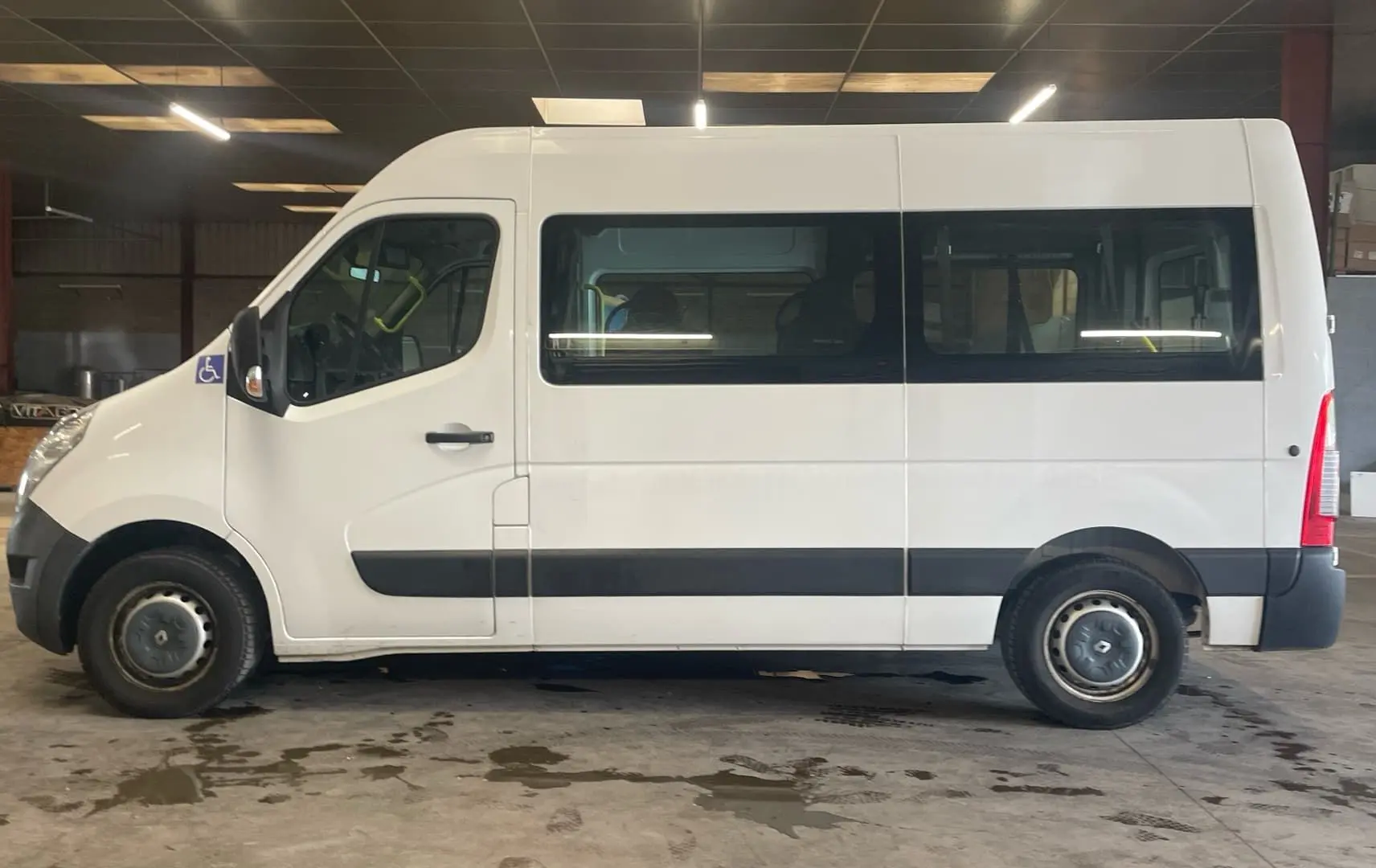 Profil latéral droit d’un Renault Master blanc TPMR 2019 avec rampe arrière et logo handicap visible près de la porte avant.