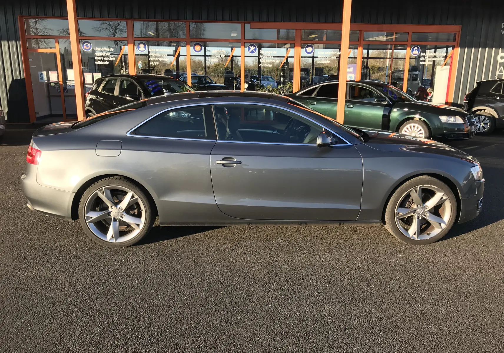 Audi A5 Coupé gris dauphin vu de profil côté gauche, avec jantes alliage 5 branches et silhouette élégante.