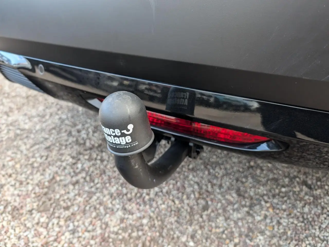 Gros plan sur l'attelage col de cygne noir à l'arrière d'une Citroën C4 rouge foncé, avec feu arrière intégré.