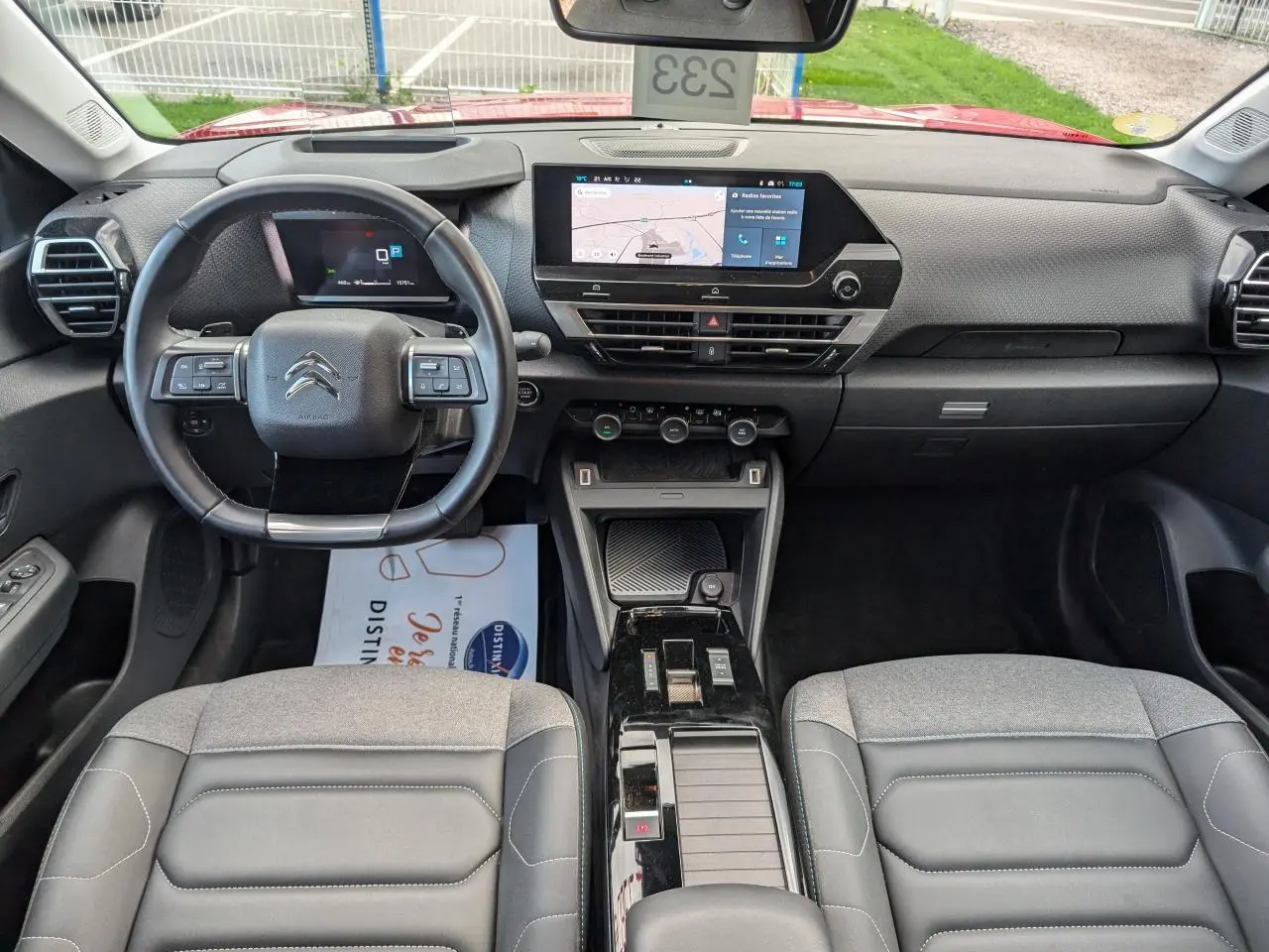 Intérieur de la Citroën C4 2024 vu de face, tableau de bord moderne avec écran tactile central et sièges gris tissu et cuir.