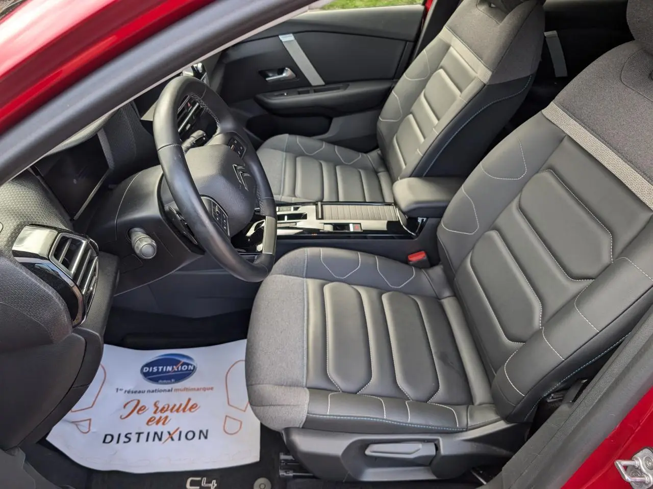 Vue intérieure côté conducteur de la Citroën C4 2024 rouge foncé, sièges Advanced Comfort gris et volant cuir noir.