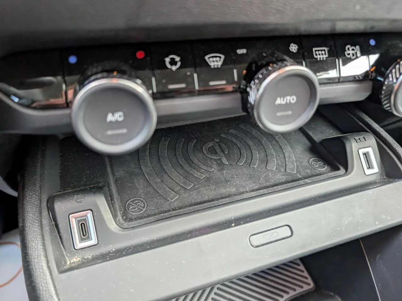 Gros plan sur la console centrale noire du Citroën C4 2024, montrant la recharge sans fil Qi et commandes climatisation.