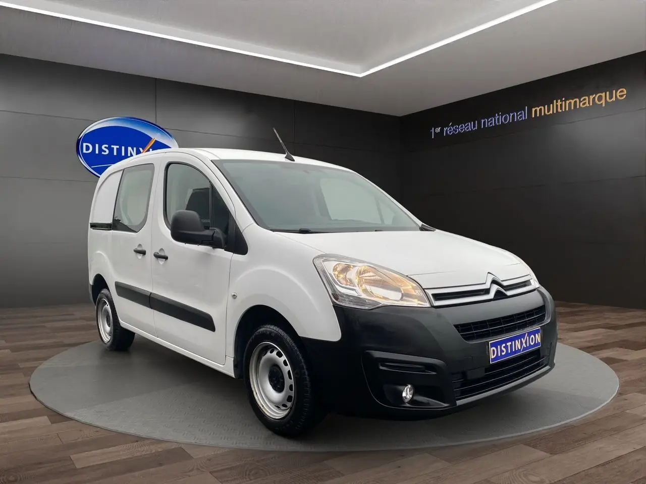Citroën Berlingo blanc vue 3/4 avant droit avec pare-chocs noir et jantes acier en showroom.