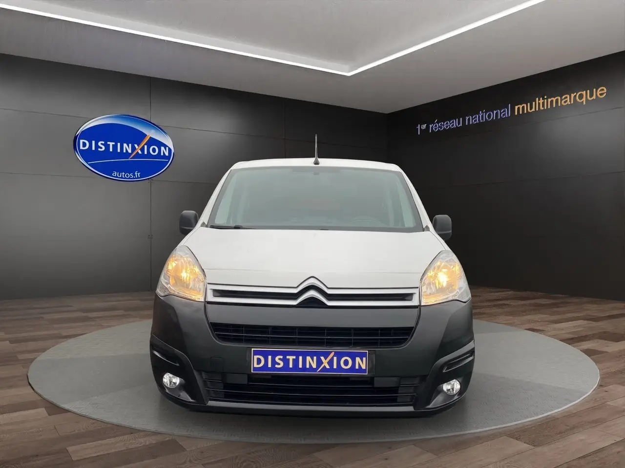 Vue de face du Citroën Berlingo blanc 2018 avec pare-chocs noir et phares allumés dans un showroom.