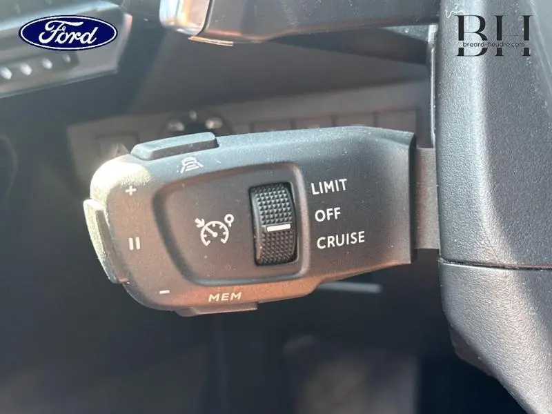 Gros plan sur la commande de régulateur de vitesse noir dans l'habitacle d'un véhicule, avec logo Ford visible.