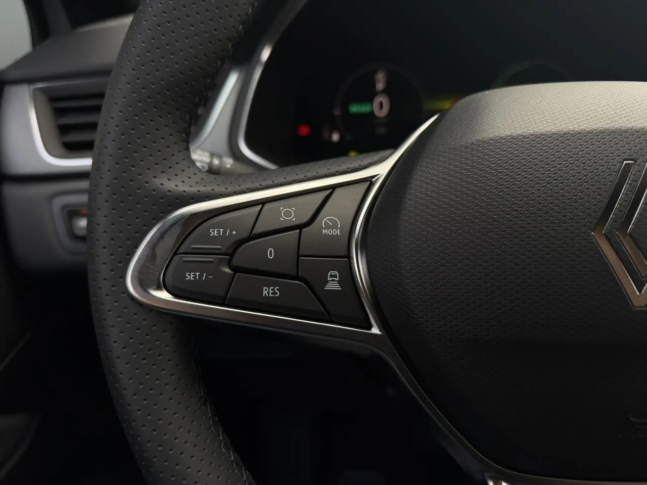Gros plan sur le volant perforé côté gauche du Renault Captur gris, avec commandes de régulateur et logo central.
