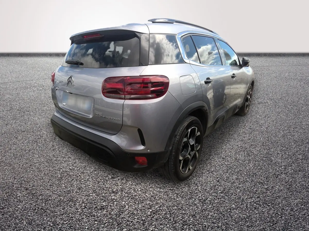 Vue 3/4 arrière droit d'un Citroën C5 gris clair hybride 2024 avec toit noir et jantes noires distinctives.