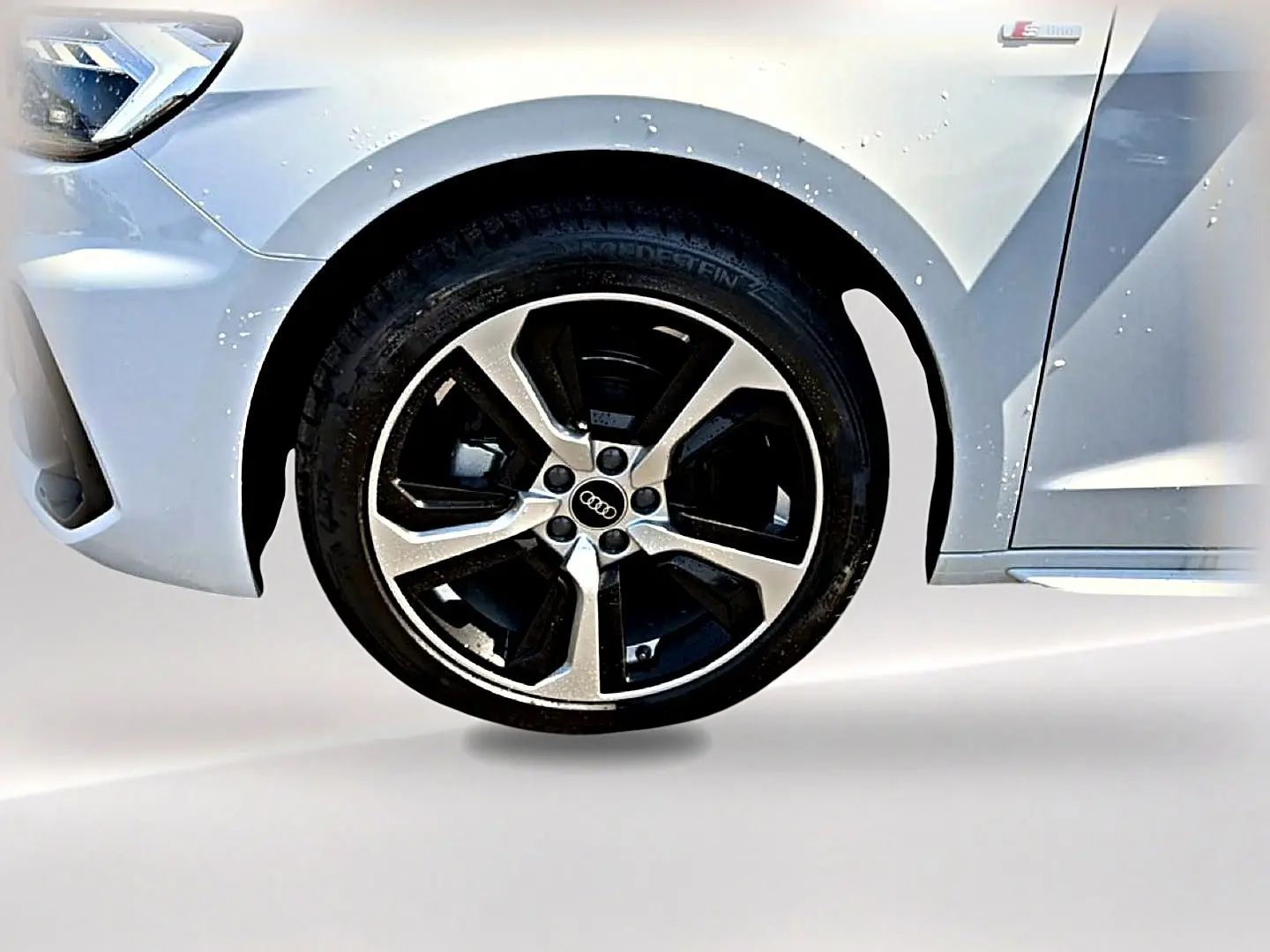 Gros plan sur la roue avant gauche d'une Audi A1 Sportback blanche avec jante alu et badge S line visible.