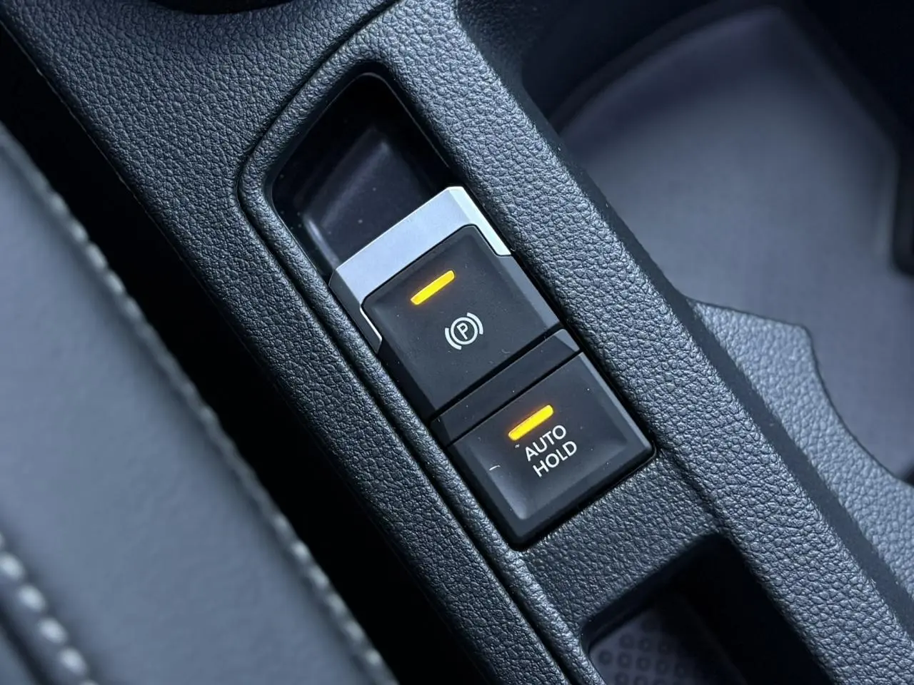Gros plan sur les commandes du frein de stationnement électromécanique et Auto Hold du Volkswagen T-Roc gris Pyrite.
