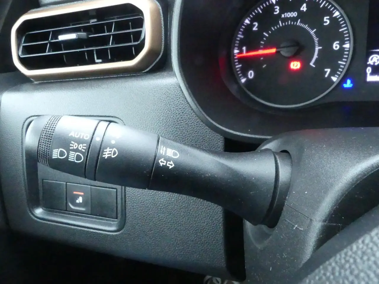 Gros plan sur la manette de commande d'éclairage et clignotants du tableau de bord noir du Dacia Duster 2023 finition Extreme.