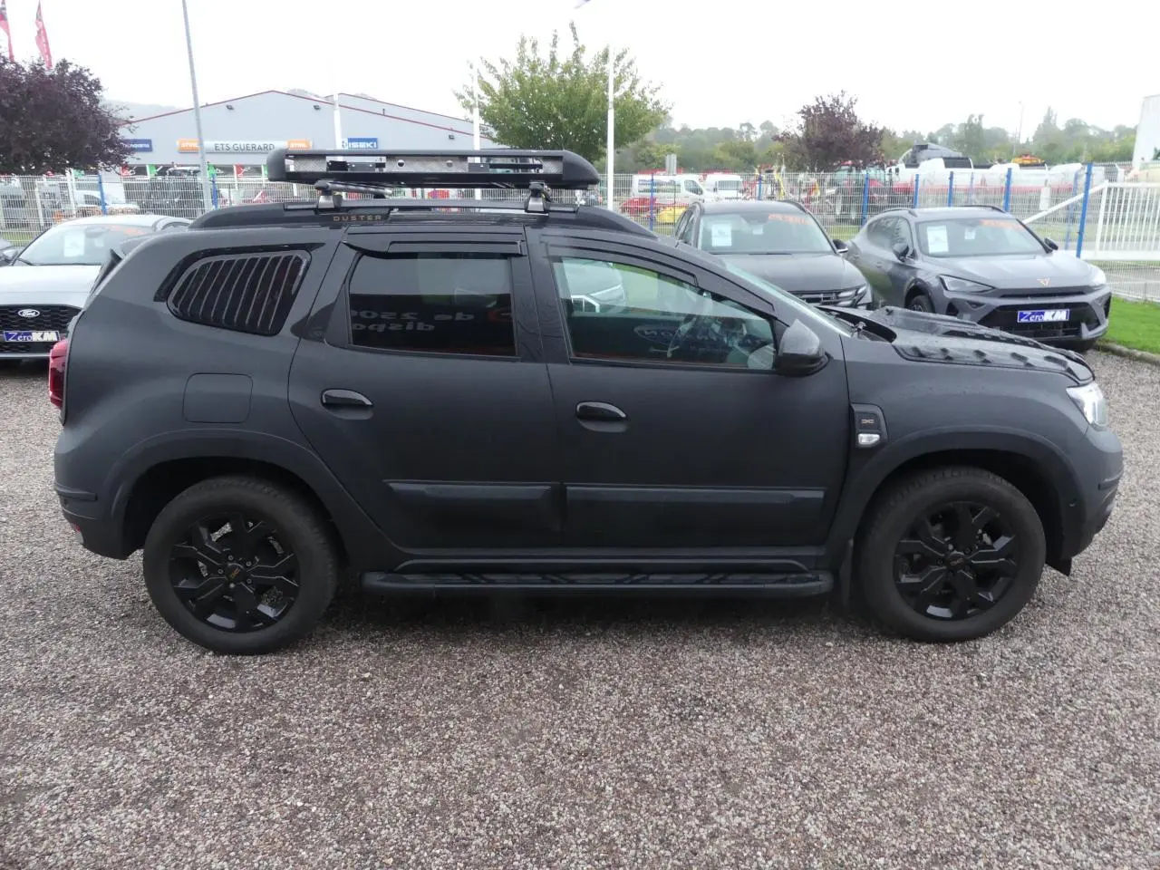 Profil côté gauche du Dacia Duster 2023 noir mat avec galerie de toit, marchepied et jantes noires.