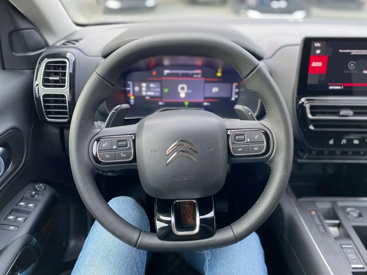 Vue intérieure centrée sur le volant noir du Citroën C5 Aircross 2025 avec tableau de bord numérique et écran tactile.