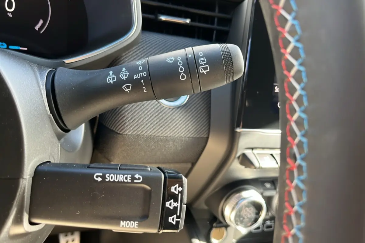 Gros plan sur le commodo gauche et volant avec surpiqûres tricolores de la Renault Clio V E-Tech 145 Esprit Alpine.