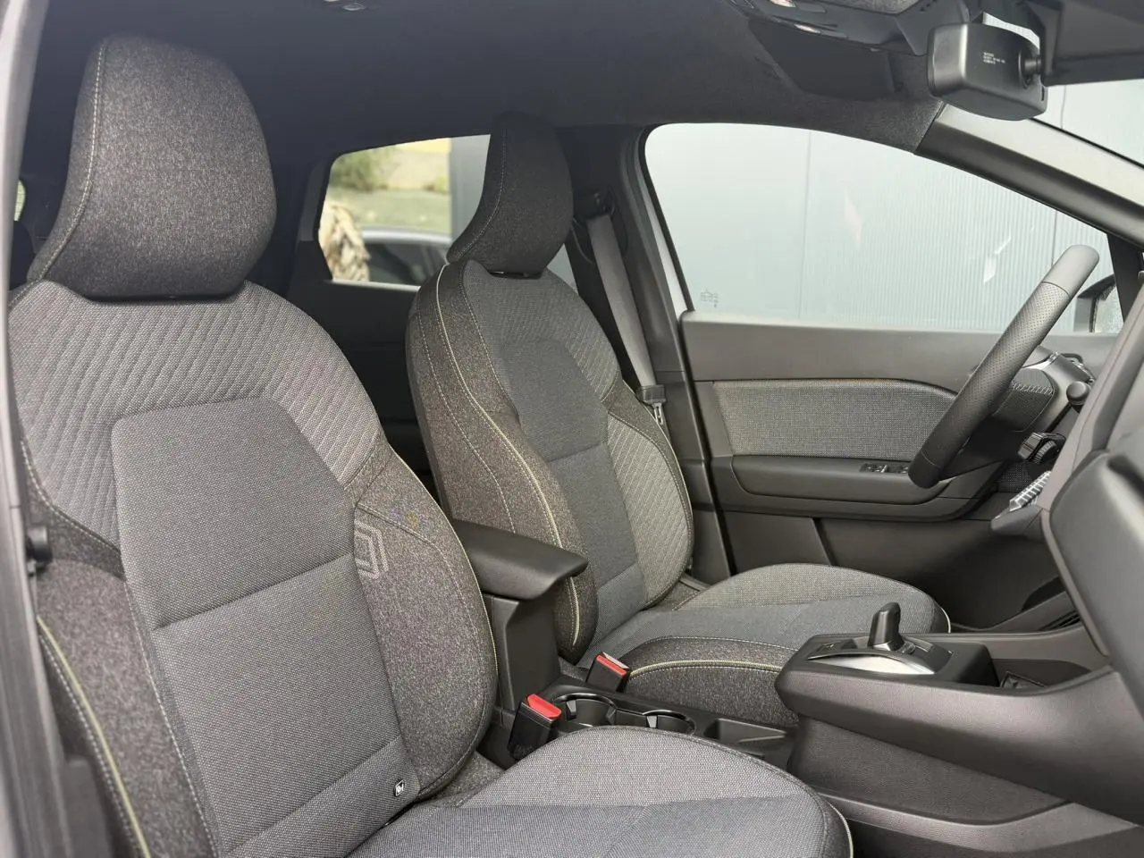 Vue intérieure côté droit du Renault Captur 2026, sièges tissu gris avec surpiqûres contrastées et console centrale.