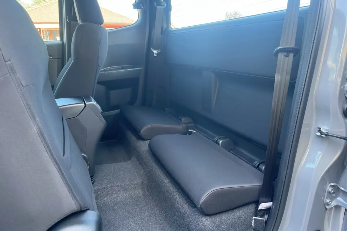 Vue intérieure côté arrière droit du pick-up Isuzu D-MAX 2026 gris Kinabalu avec strapontins rabattus et sièges tissu noirs.
