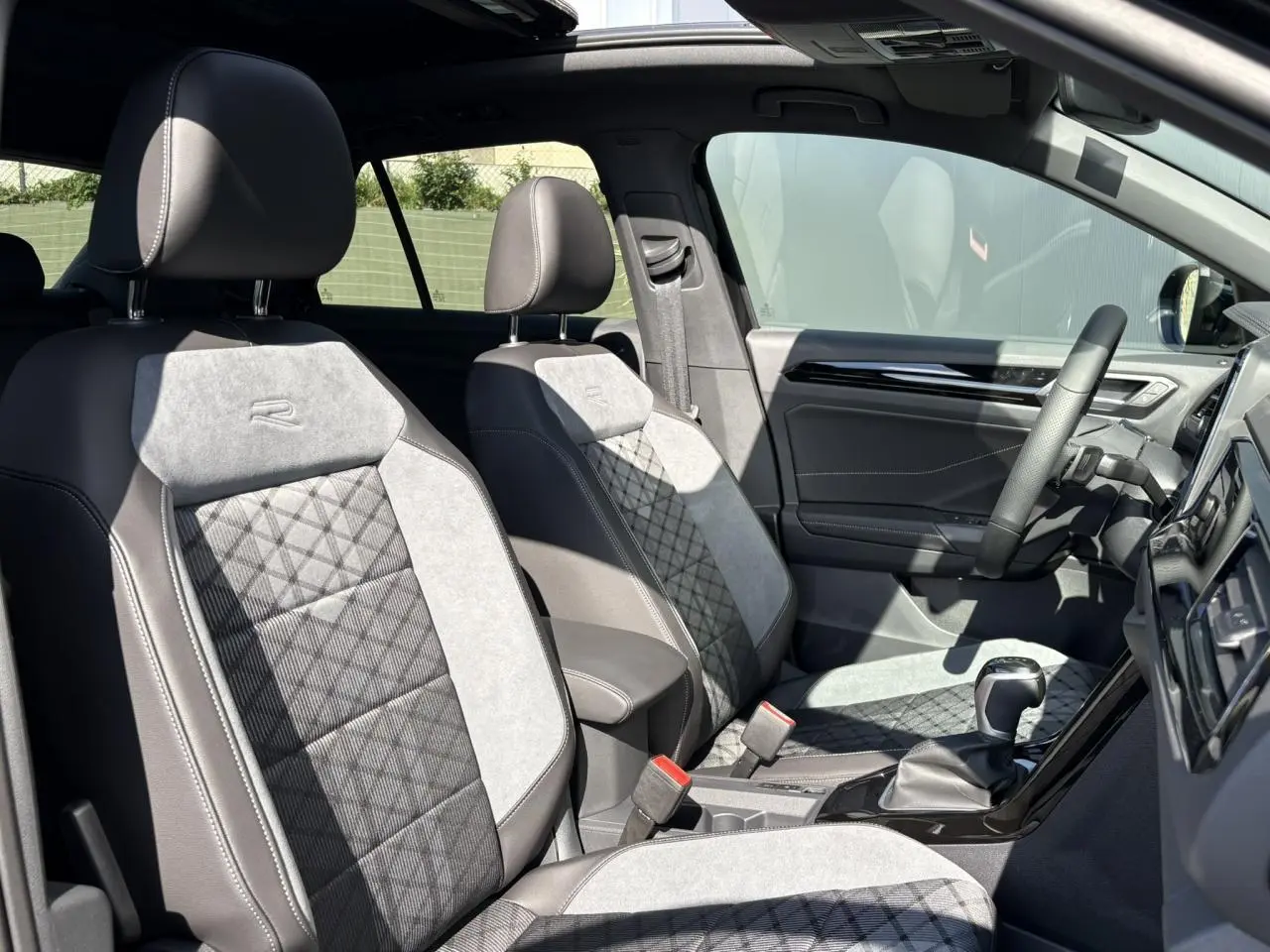 Intérieur avant du Volkswagen T-Roc 2025 avec sièges R-Line gris et noir, volant cuir et toit ouvrant visible.