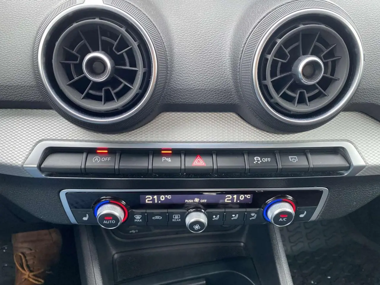 Détail de la console centrale de l’Audi Q2 noire 2023, avec commandes climatisation automatique et aérateurs ronds.
