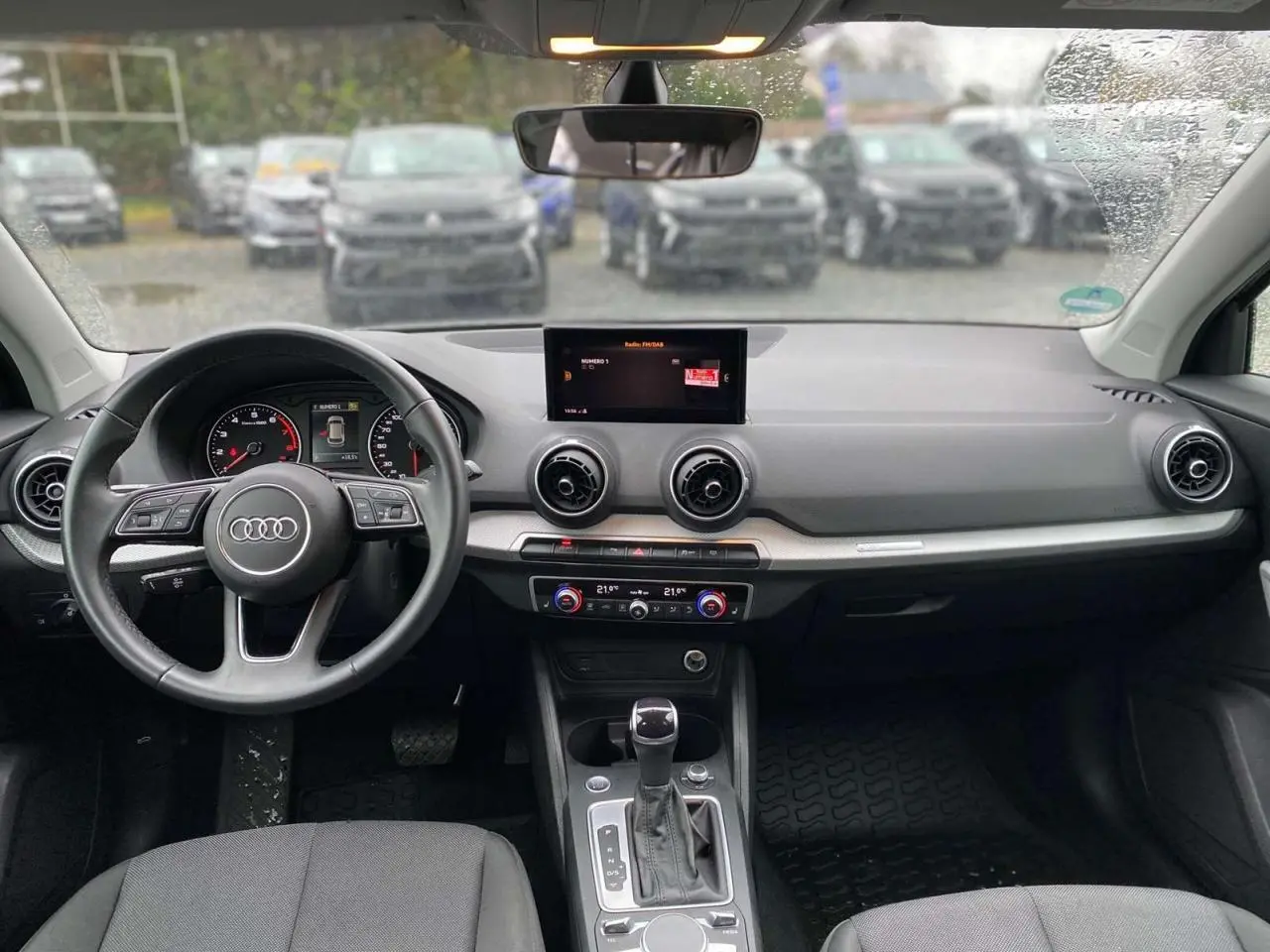 Vue intérieure avant de l'Audi Q2 2023 noire, tableau de bord avec écran central, volant multifonction et climatisation automatique.