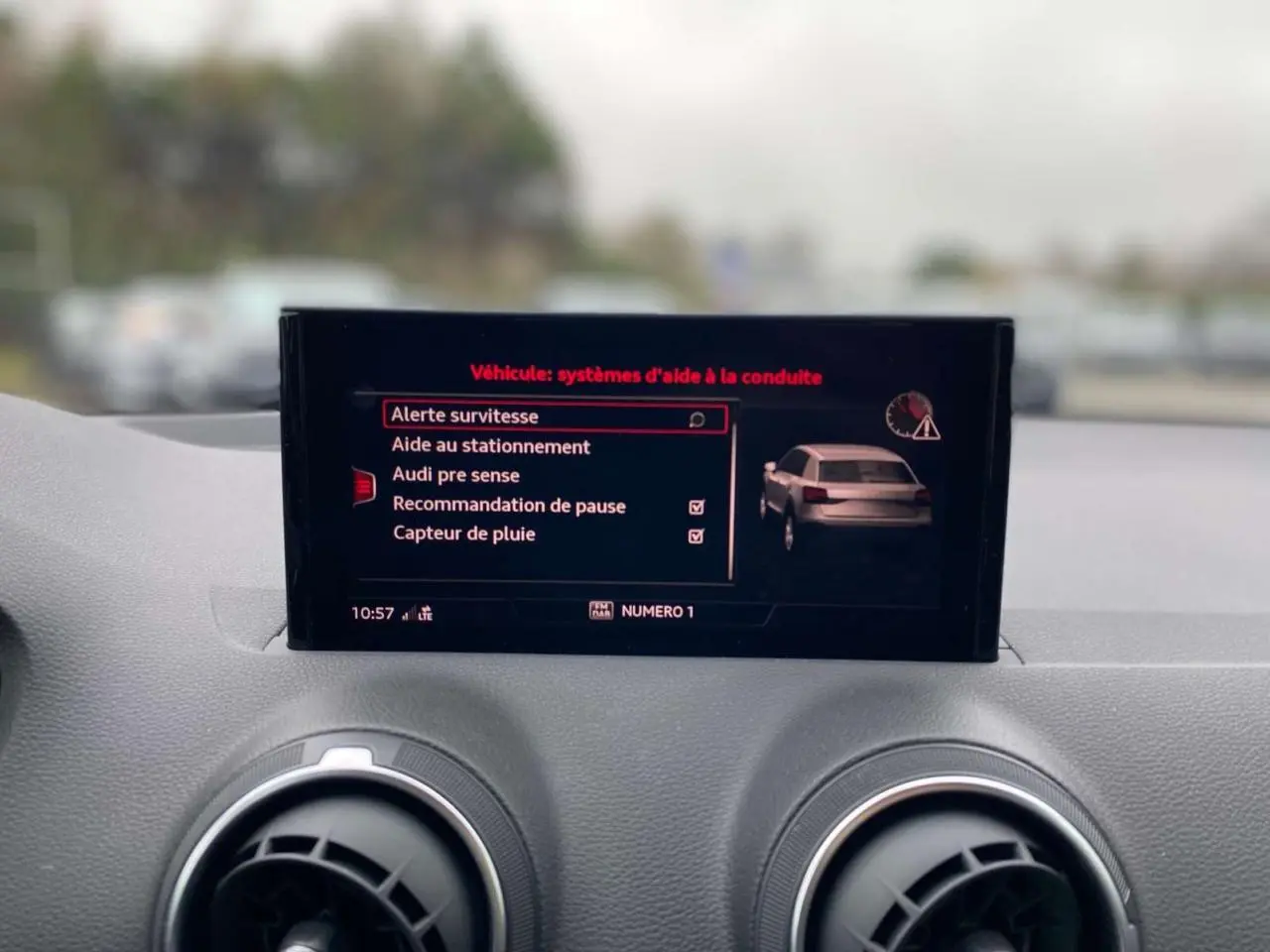 Écran central de l'Audi Q2 2023 affichant les aides à la conduite, avec tableau de bord gris en arrière-plan.