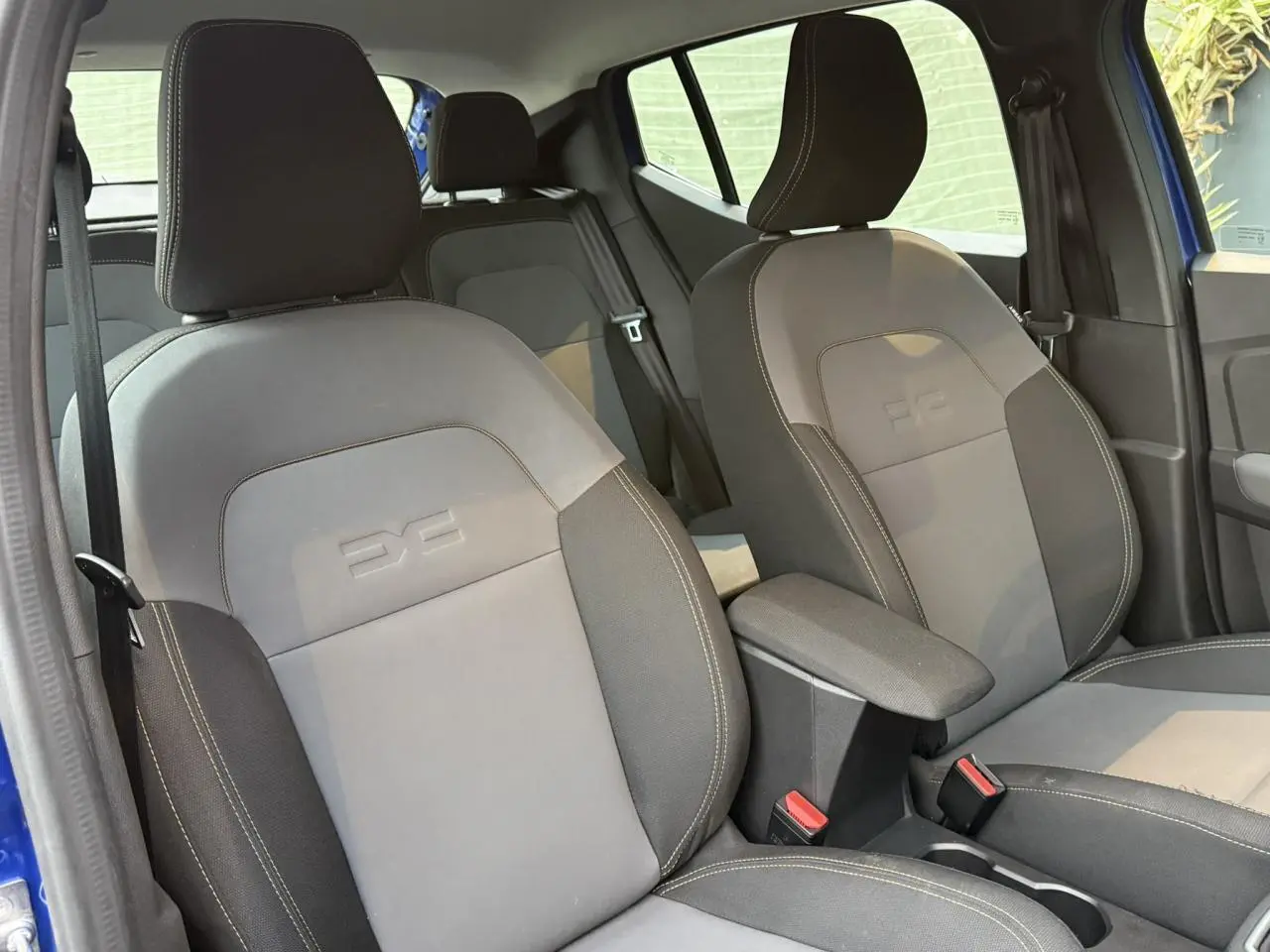 Vue intérieure montrant les sièges avant gris avec logo DC embossé et accoudoir central de la Dacia Sandero Stepway Bleu Iron.
