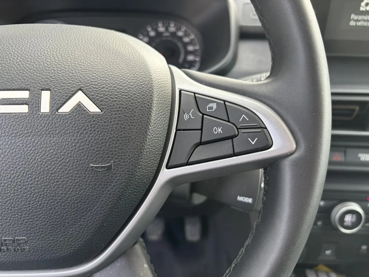 Gros plan sur le volant noir de la Dacia Sandero Stepway 2025, avec commandes multifonctions et logo Dacia visible.