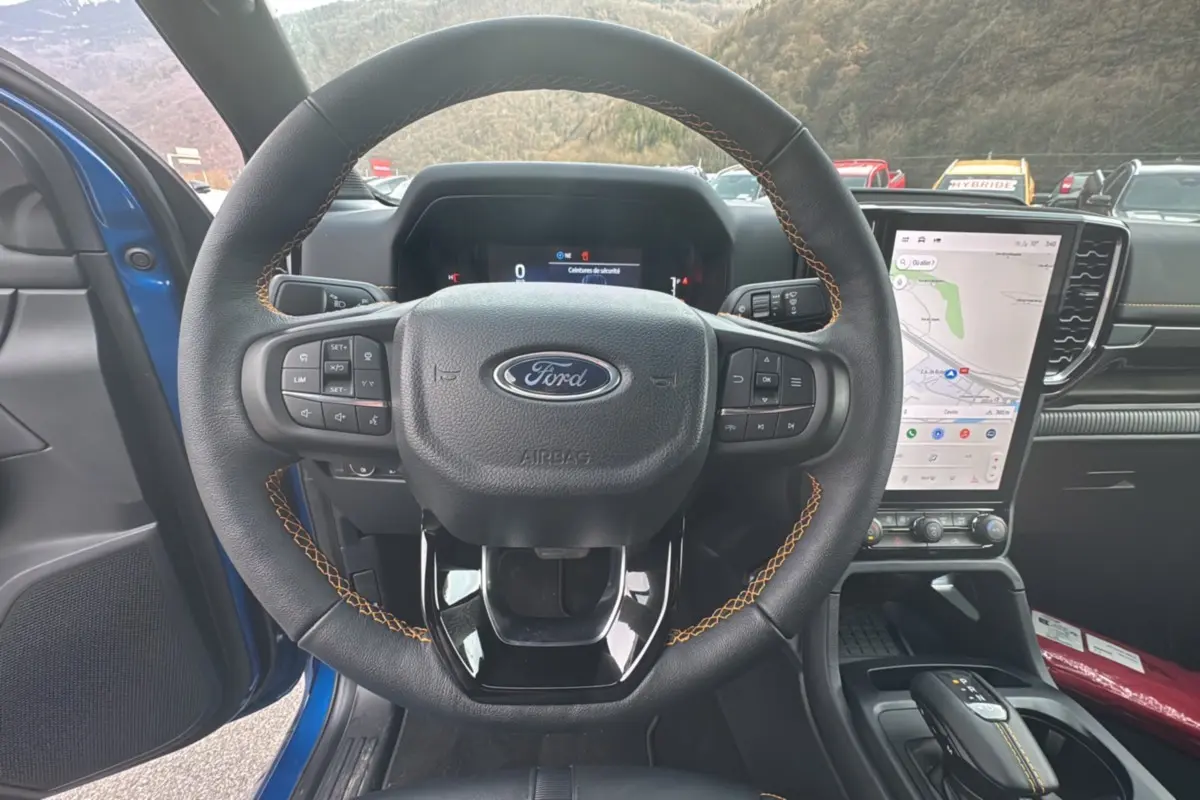 Vue intérieure centrée sur le volant cuir noir avec surpiqûres orange du Ford Ranger Wildtrak 2025 bleu lightning.