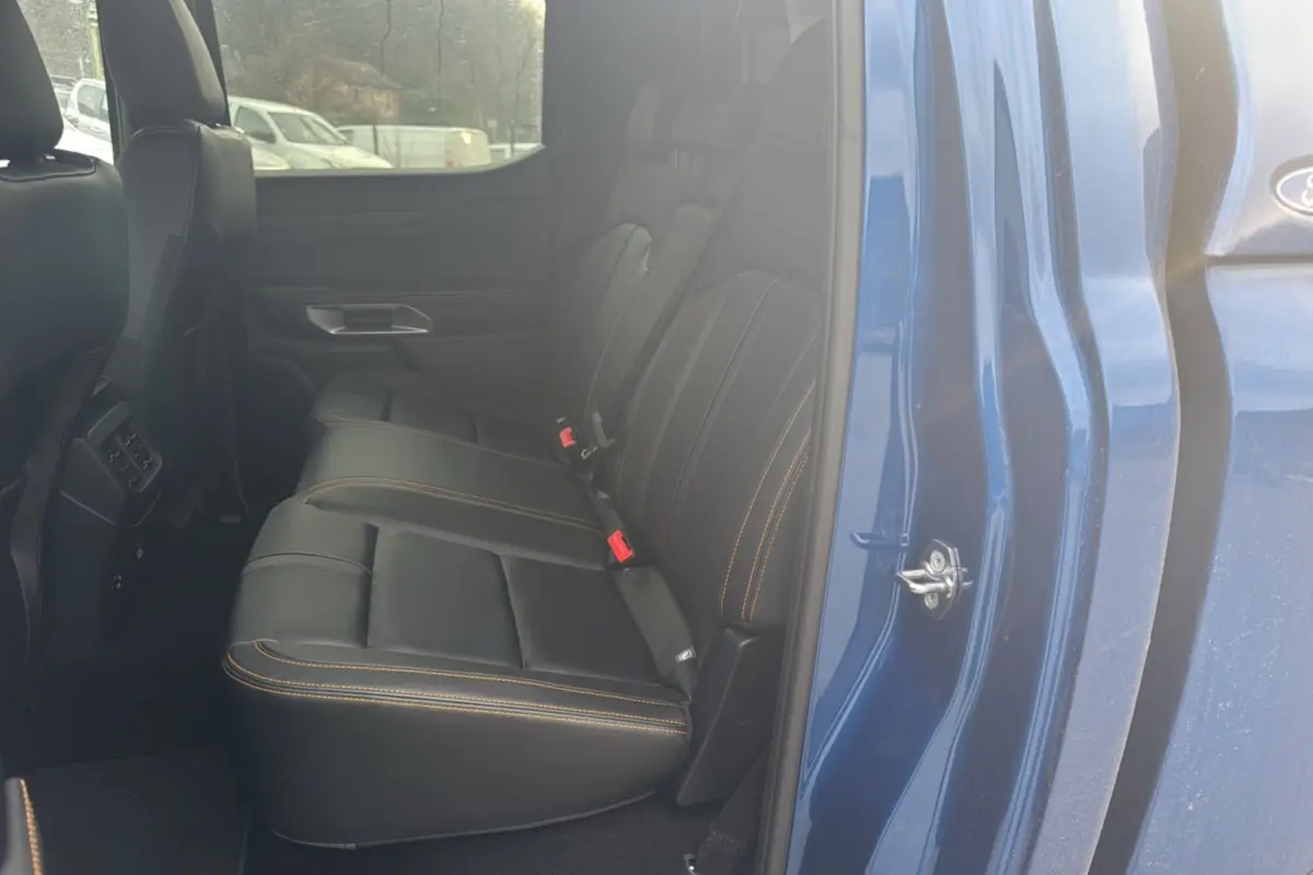 Vue intérieure côté arrière droit du Ford Ranger 3.0 V6 Wildtrak bleu lightning, sièges cuir noirs avec surpiqûres orange.