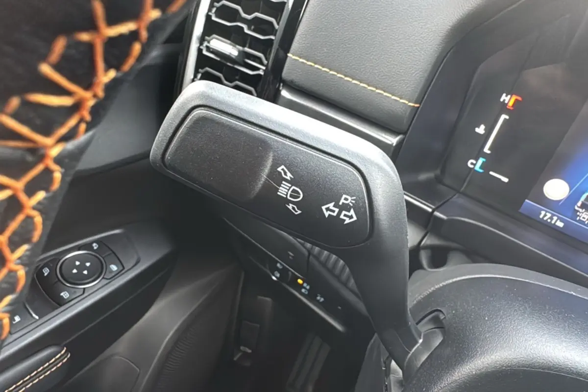 Gros plan sur la manette de clignotants et les commandes au volant avec surpiqûres orange dans l’habitacle noir du Ford Ranger Wildtrak.