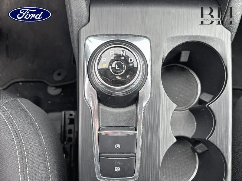 Vue plongeante sur la console centrale grise du Ford Kuga 2023, avec molette de boîte auto et porte-gobelets.