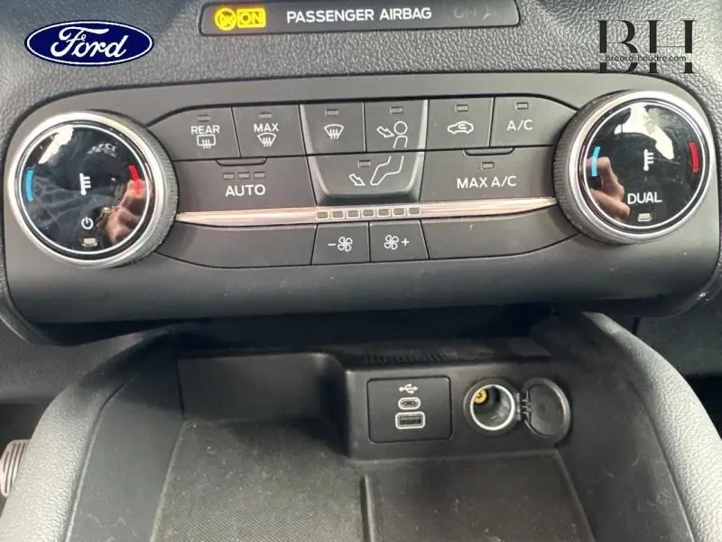 Vue rapprochée de la console centrale du Ford Kuga 2023, montrant les commandes de climatisation et prises USB et 12V.