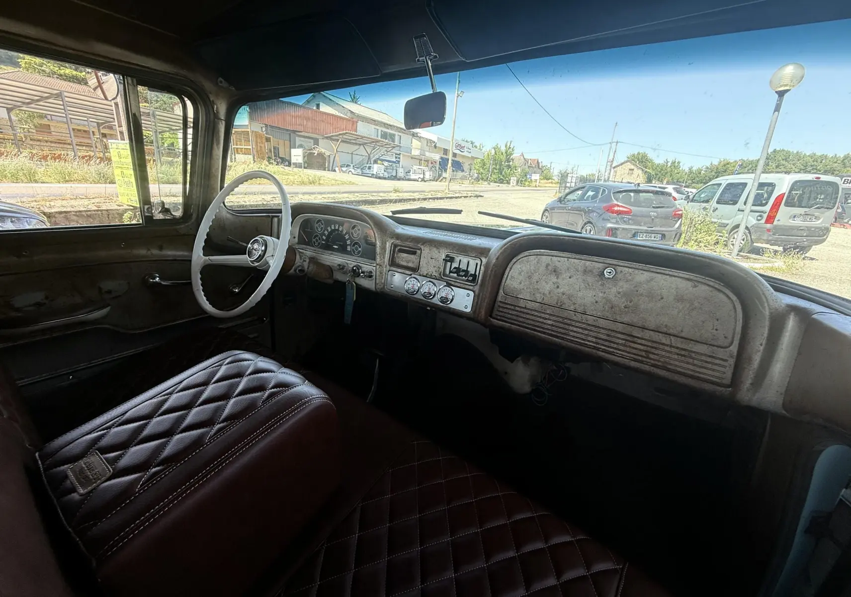 Vue intérieure côté conducteur du tableau de bord et volant blanc d’un Chevrolet C10 Apache 1963 avec sellerie marron matelassée.