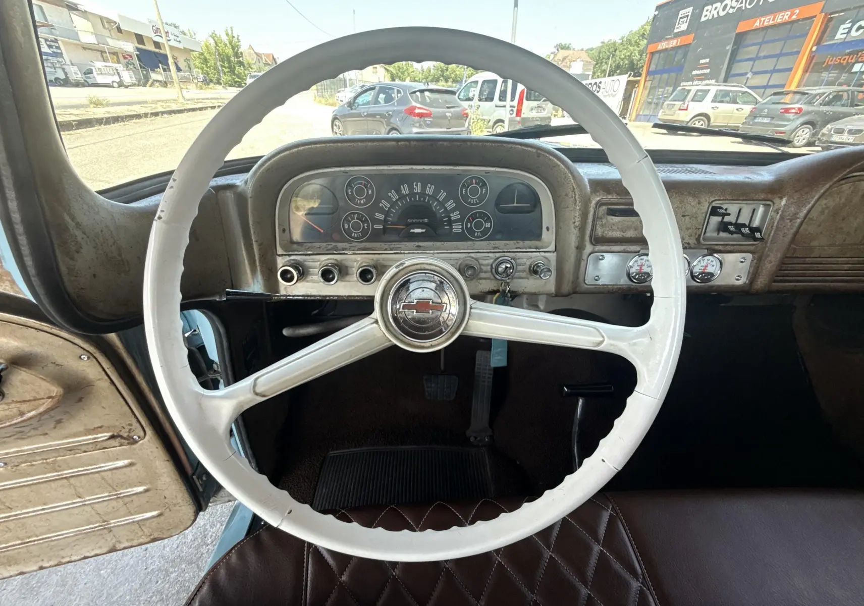 Vue intérieure centrée sur le volant blanc et le tableau de bord patiné du Chevrolet C10 Apache 1963 bleu.