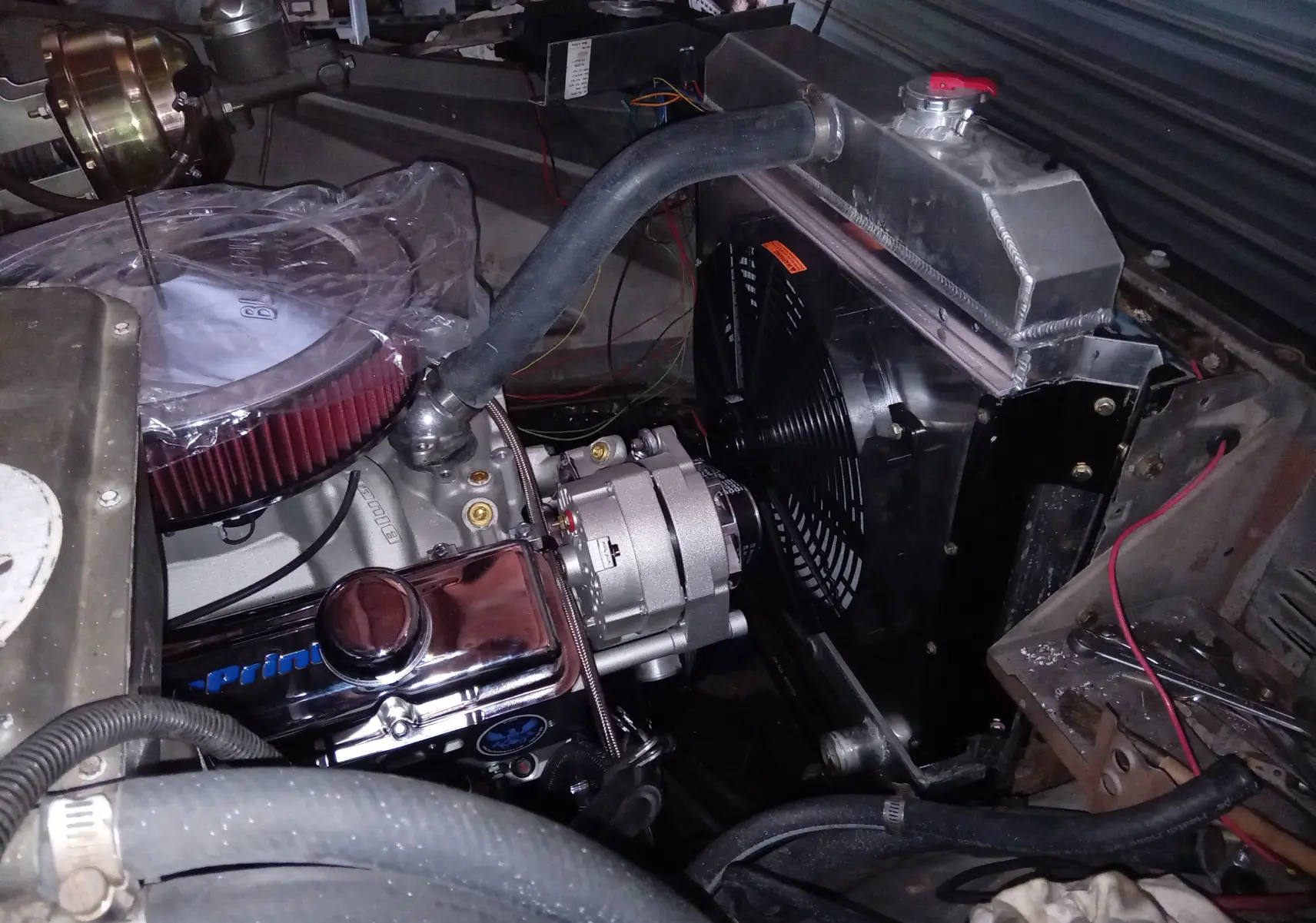Gros plan sur le moteur V8 350ci d'une Chevrolet C10 Apache 1963, avec filtre à air rouge et durites visibles.