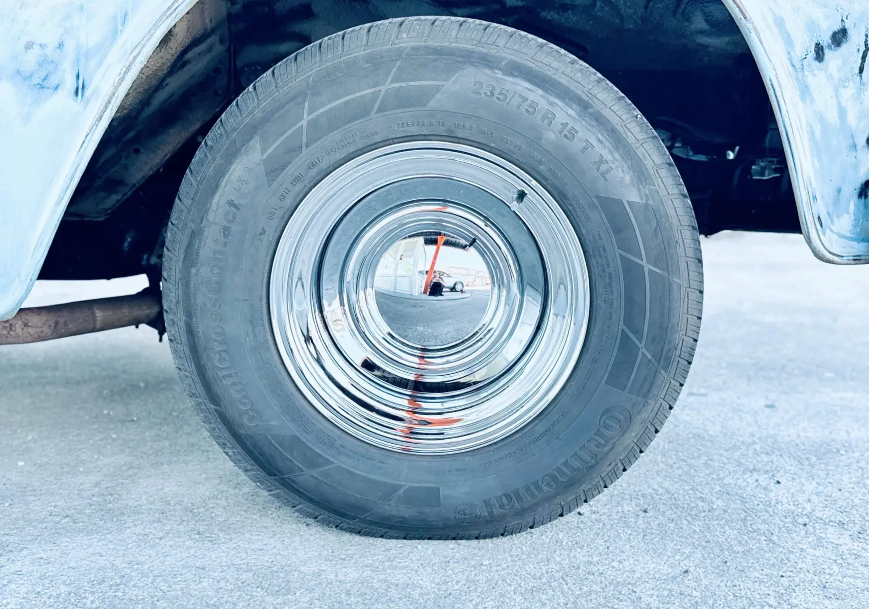 Gros plan sur la roue arrière droite chromée du Chevrolet C10 Apache 1963 bleu, avec partie de la carrosserie visible.