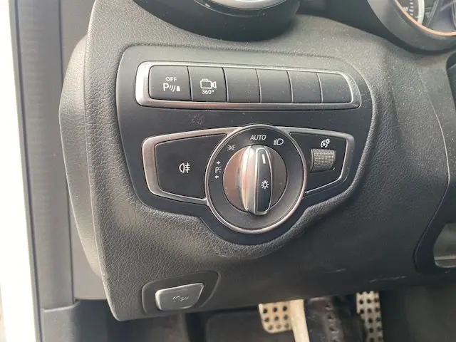 Gros plan sur le bouton de commande des phares et des aides à la conduite dans l'habitacle noir d'une Mercedes Classe C 250D 2018.