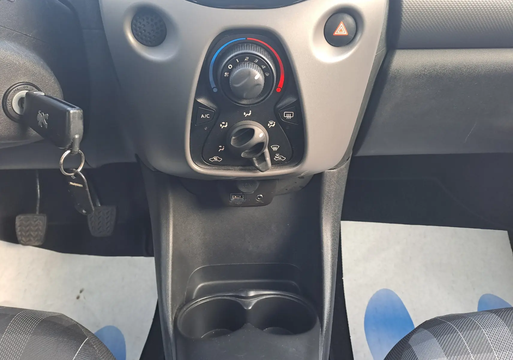 Vue rapprochée du tableau de bord central et de la console d'une Peugeot 108 noire, avec clés au contact et commandes de climatisation.