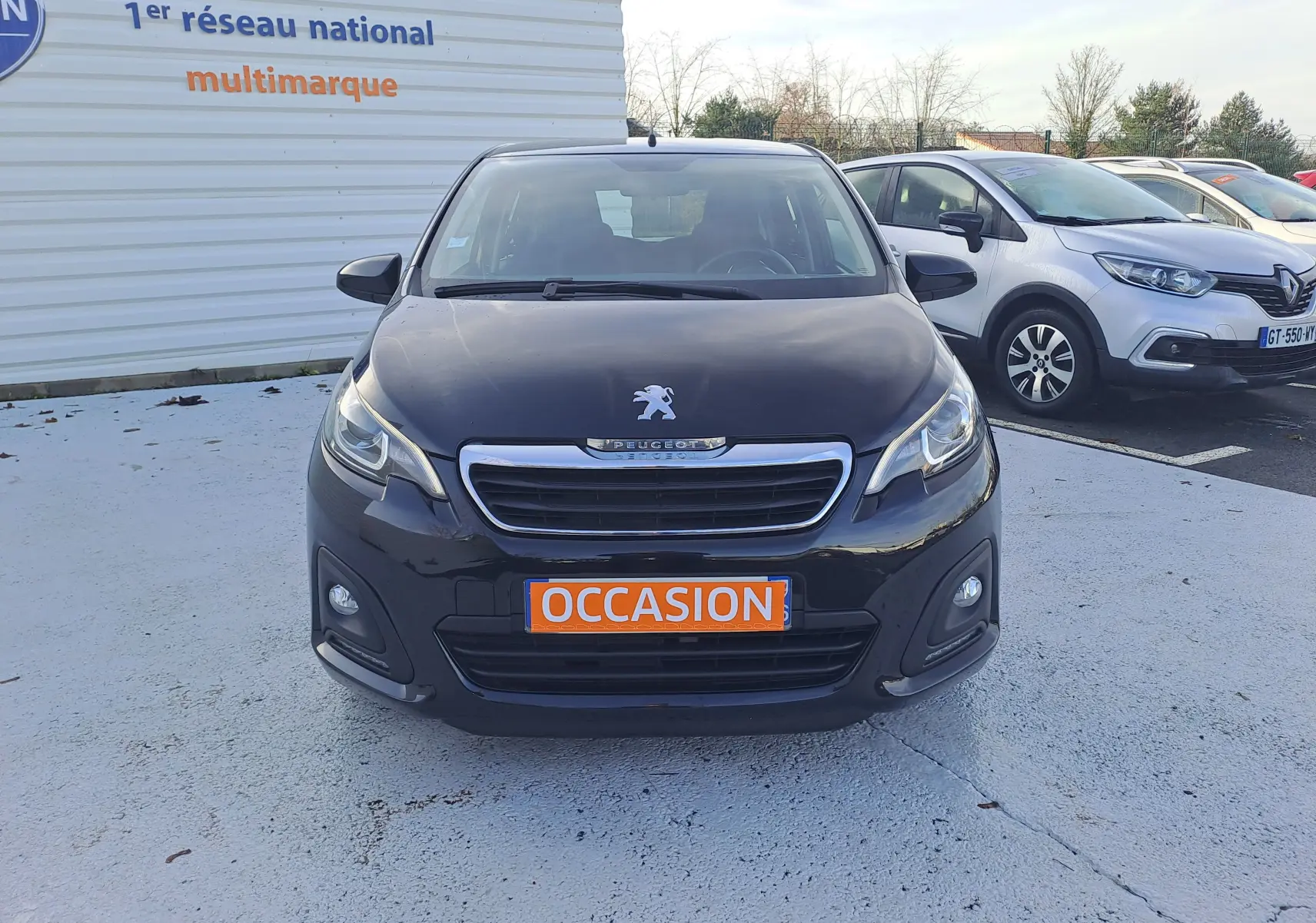 Vue frontale d'une Peugeot 108 noire de 2020 avec plaque "OCCASION" et phares LED allumés sur parking.