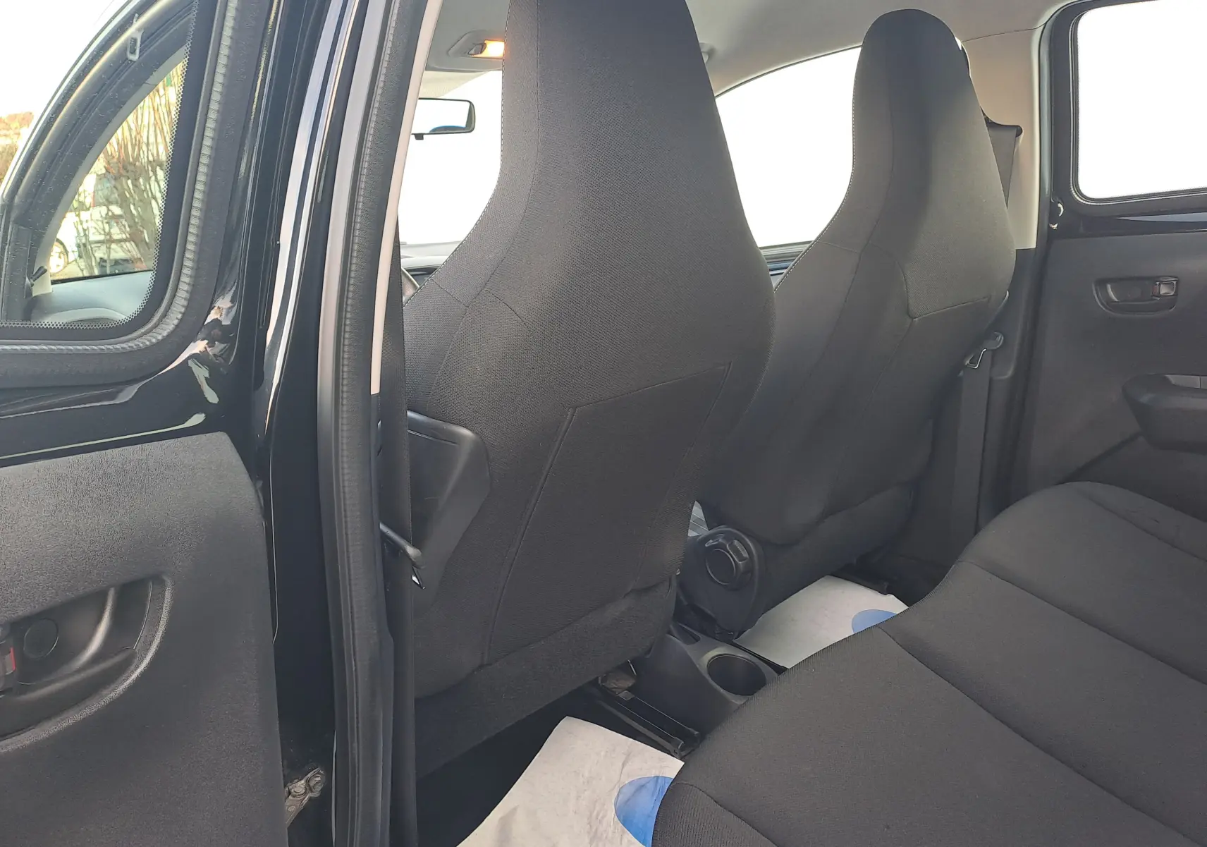 Vue intérieure arrière côté gauche d'une Peugeot 108 noire, montrant les sièges en tissu noir et la porte arrière ouverte.