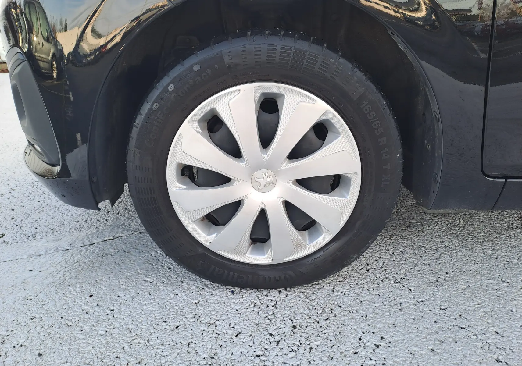 Gros plan sur la roue avant gauche noire d'une Peugeot 108 2020 avec enjoliveur argenté et logo lion central.